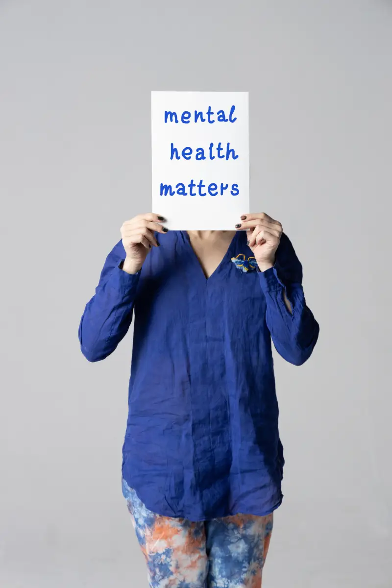 Woman covering her face with a white poster with the words mental health matter.<br />